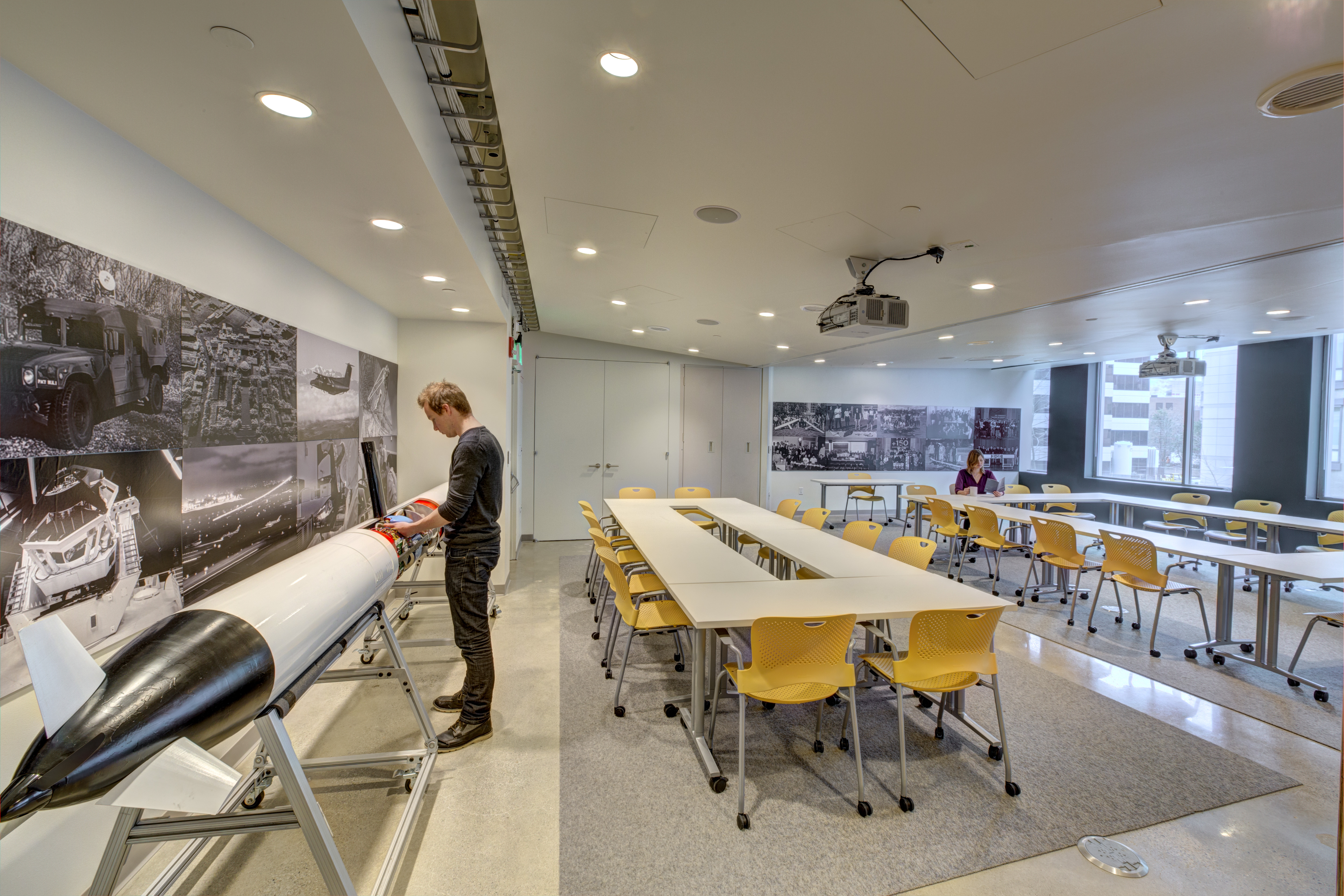 The image shows a large classroom with two long tables surrounded by chairs.