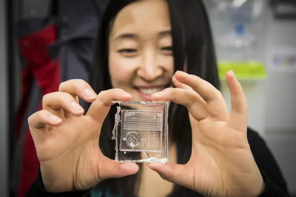 A 10th grade girl holds a see-through 3D-printed item containing a circuit board.