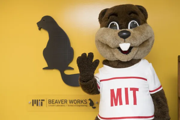 Beaver Works mascot standing in front of a yellow wall with the Beaver Works logo