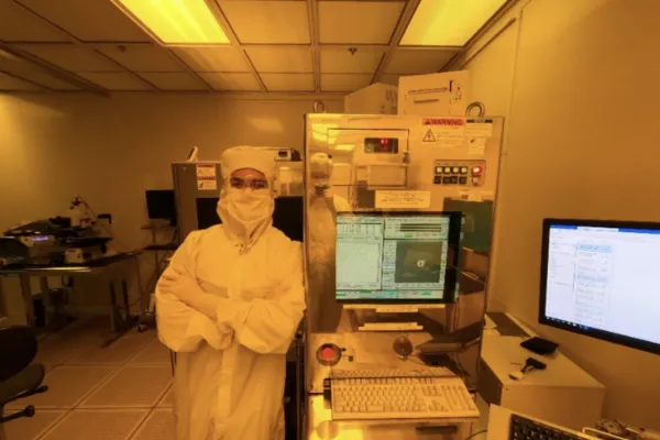 an intern dressed in a "bunny suit" leans against a machine in the microelectronics laboratory.