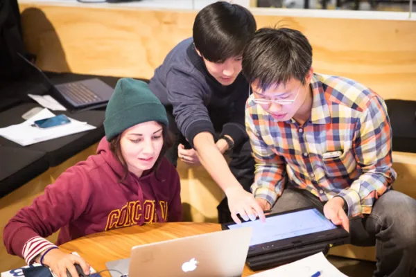 A group of three students compare their laptop screens as they work on a team project in the collaboration space at Beaver Works. 
