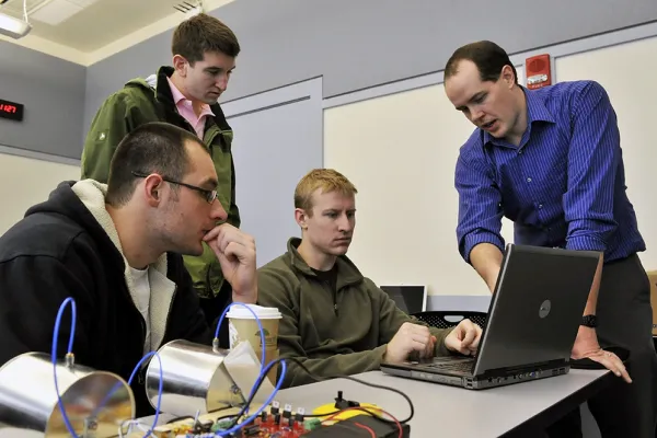 An instructor is showing three students something on a laptop